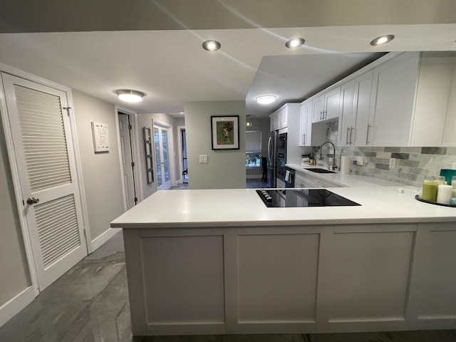 kitchen with kitchen peninsula, decorative backsplash, black electric cooktop, sink, and white cabinetry