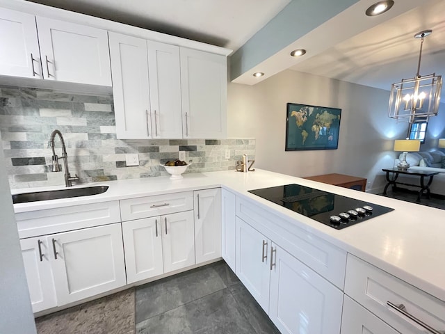 kitchen with black electric stovetop, tasteful backsplash, sink, white cabinets, and hanging light fixtures