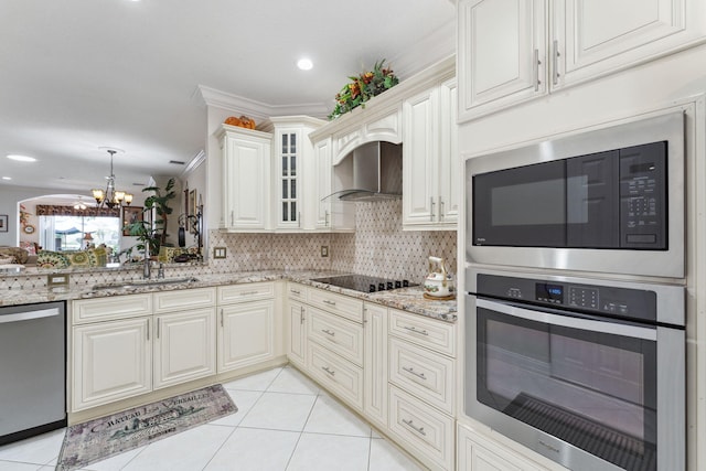 kitchen with wall chimney range hood, light tile patterned floors, appliances with stainless steel finishes, light stone counters, and decorative backsplash