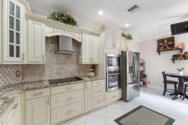 kitchen with wall chimney exhaust hood, appliances with stainless steel finishes, and cream cabinetry