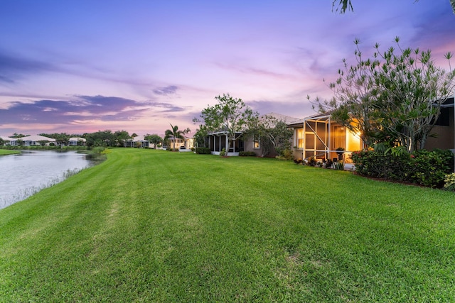 yard at dusk with a water view and glass enclosure