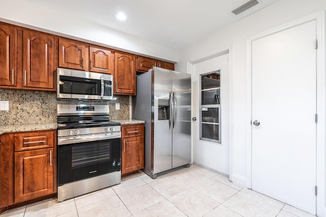 kitchen featuring light stone counters, light tile patterned floors, appliances with stainless steel finishes, and tasteful backsplash