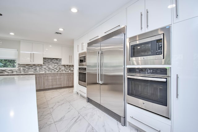 kitchen featuring light tile patterned flooring, white cabinets, built in appliances, and tasteful backsplash