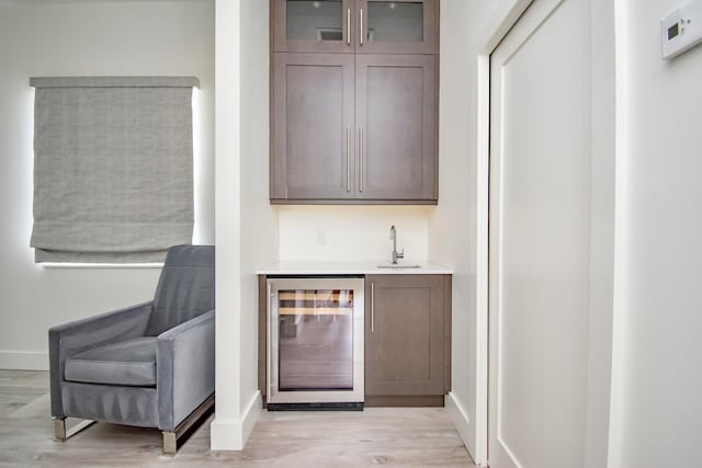 bar with sink, light hardwood / wood-style flooring, wine cooler, and dark brown cabinetry