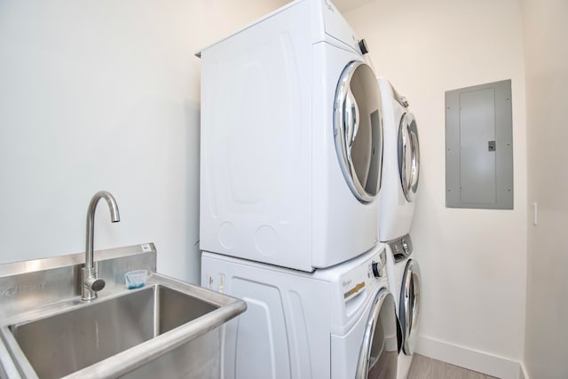 clothes washing area featuring stacked washer / drying machine, sink, light hardwood / wood-style flooring, and electric panel