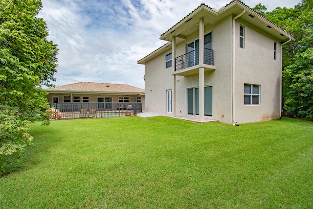 rear view of house featuring a patio area, a balcony, and a lawn