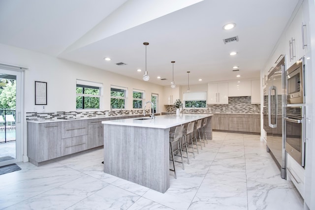 kitchen featuring light tile patterned floors, a spacious island, decorative backsplash, white cabinetry, and stainless steel appliances