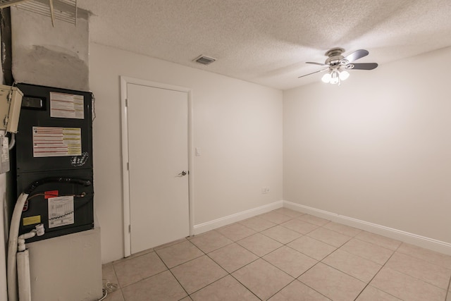 tiled spare room featuring ceiling fan, a textured ceiling, and heating unit