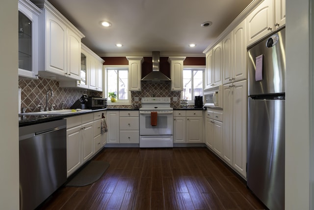 kitchen with appliances with stainless steel finishes, wall chimney exhaust hood, white cabinetry, tasteful backsplash, and sink