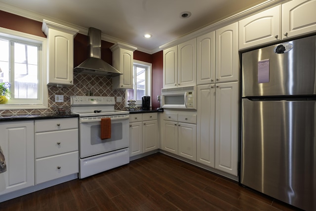 kitchen with wall chimney exhaust hood, dark wood-type flooring, tasteful backsplash, white appliances, and ornamental molding