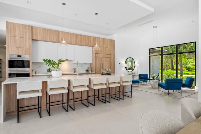 kitchen with decorative backsplash, stainless steel double oven, a kitchen bar, a large island, and decorative light fixtures