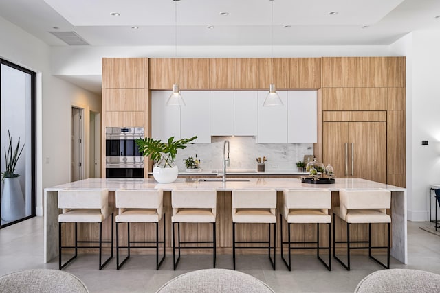 kitchen with a breakfast bar, sink, double oven, white cabinetry, and a large island with sink