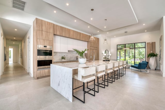 kitchen with stainless steel double oven, tasteful backsplash, a large island with sink, a breakfast bar area, and hanging light fixtures