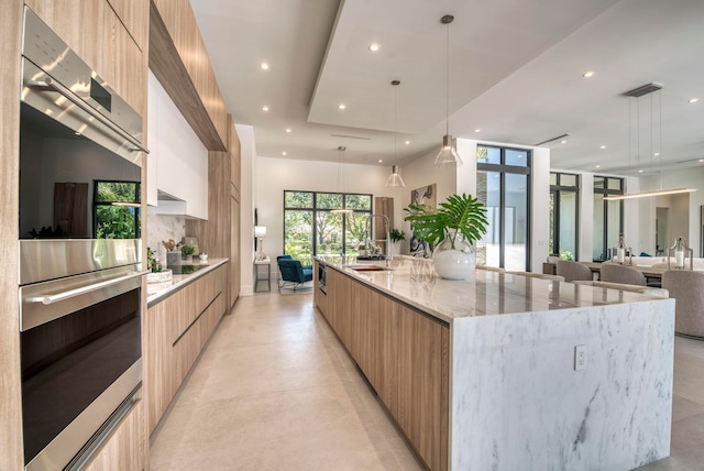 kitchen with pendant lighting, a spacious island, light stone counters, sink, and double oven