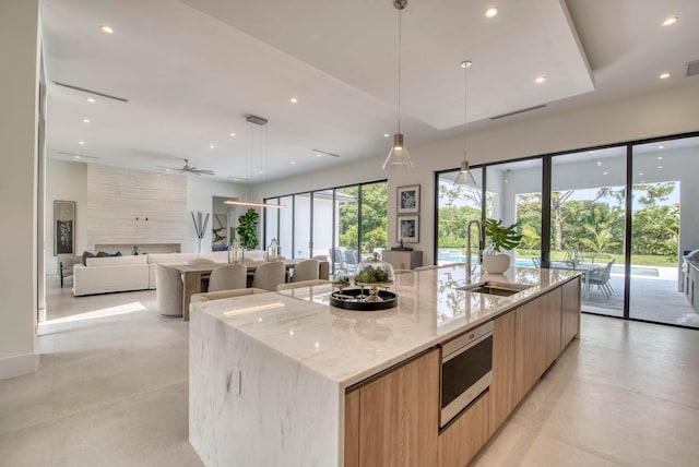 kitchen with decorative light fixtures, a large island, sink, light stone countertops, and ceiling fan