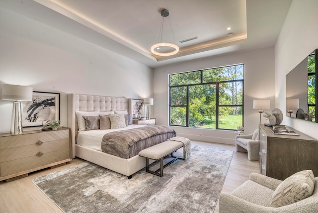 bedroom with multiple windows, a raised ceiling, and light hardwood / wood-style floors