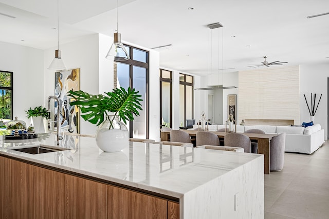 kitchen with sink, light stone counters, ceiling fan, and hanging light fixtures