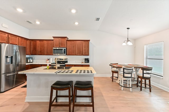 kitchen featuring a center island with sink, stainless steel appliances, lofted ceiling, and light hardwood / wood-style flooring