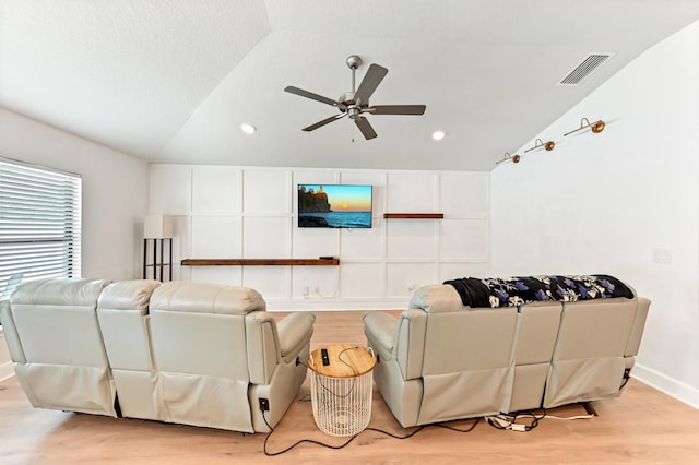 living room featuring ceiling fan, light wood-type flooring, lofted ceiling, and a textured ceiling