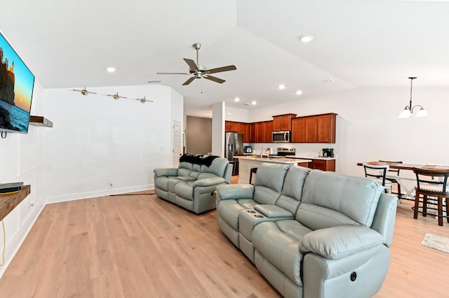 living room with ceiling fan with notable chandelier, vaulted ceiling, and light wood-type flooring