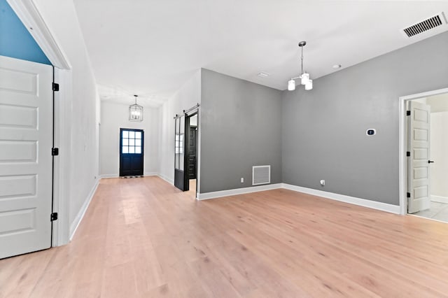 foyer featuring a barn door, light wood-type flooring, and a chandelier