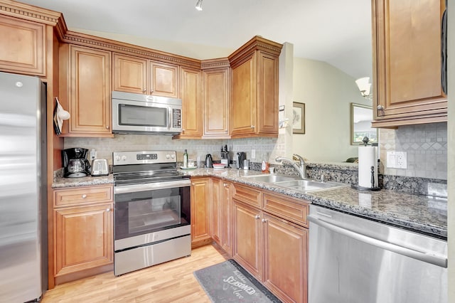 kitchen with sink, vaulted ceiling, light wood-type flooring, appliances with stainless steel finishes, and tasteful backsplash