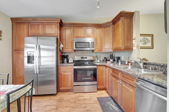 kitchen featuring light stone countertops, appliances with stainless steel finishes, light wood-type flooring, decorative backsplash, and sink