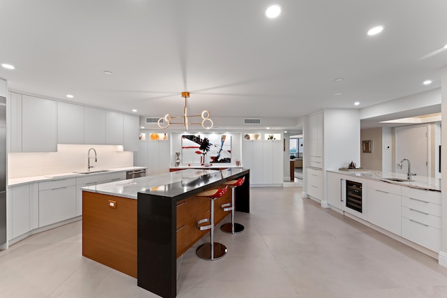 kitchen with beverage cooler, pendant lighting, white cabinets, a center island, and light stone countertops