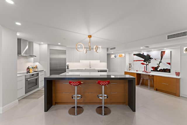 kitchen with light tile patterned flooring, white cabinetry, wall chimney range hood, appliances with stainless steel finishes, and decorative light fixtures