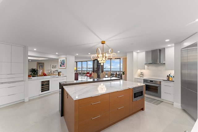 kitchen featuring built in appliances, white cabinets, wall chimney exhaust hood, light stone counters, and wine cooler