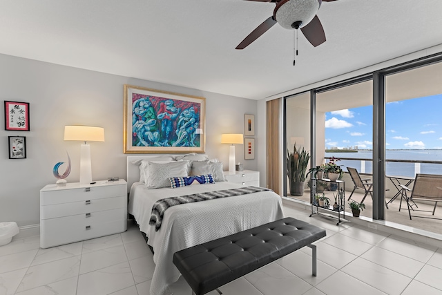 bedroom with light tile patterned flooring, ceiling fan, a water view, access to exterior, and floor to ceiling windows