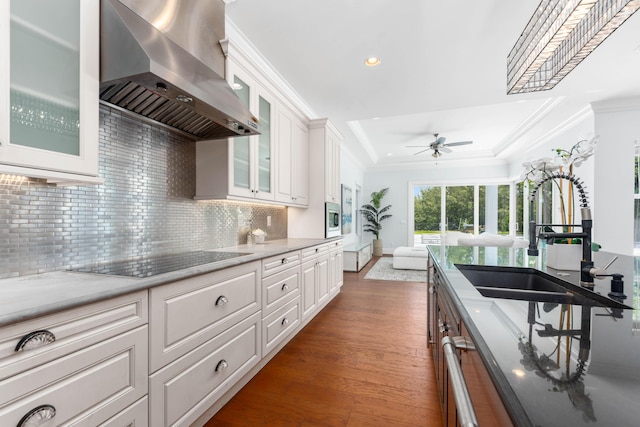 kitchen featuring black electric stovetop, backsplash, wall chimney exhaust hood, dark wood-type flooring, and white cabinets