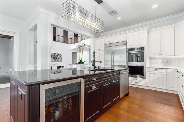 kitchen with appliances with stainless steel finishes, beverage cooler, sink, a center island with sink, and an inviting chandelier