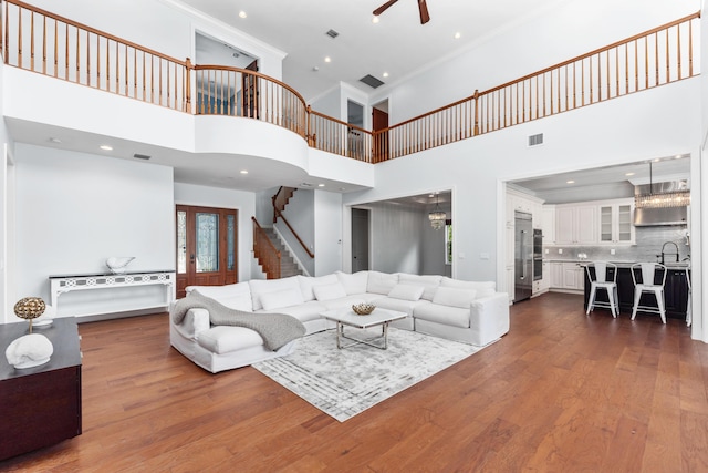 living room with ceiling fan, sink, dark wood-type flooring, a towering ceiling, and ornamental molding