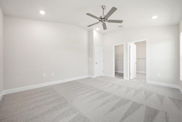 unfurnished bedroom featuring ceiling fan, light colored carpet, vaulted ceiling, a walk in closet, and a closet