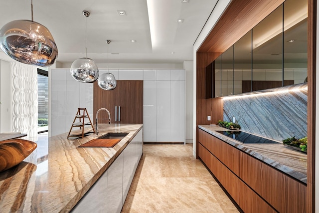 kitchen featuring black electric cooktop, light stone countertops, sink, and hanging light fixtures