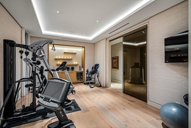 workout room with a raised ceiling and light wood-type flooring