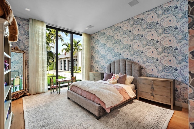 bedroom with access to exterior, light hardwood / wood-style flooring, and a wall of windows