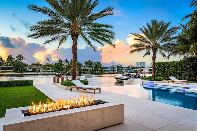 pool at dusk featuring a water view, an outdoor fire pit, and a patio