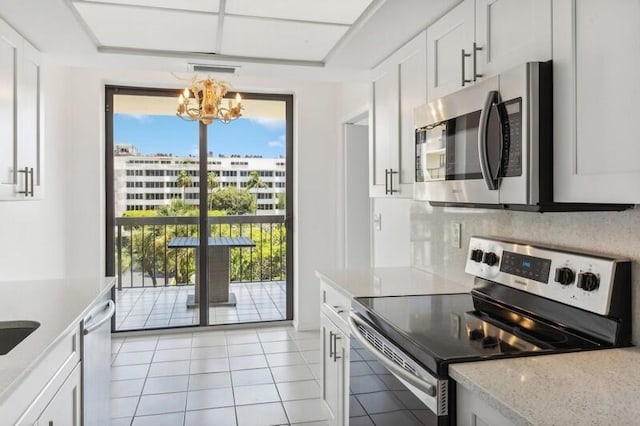 kitchen featuring light stone countertops, light tile patterned floors, an inviting chandelier, white cabinets, and appliances with stainless steel finishes