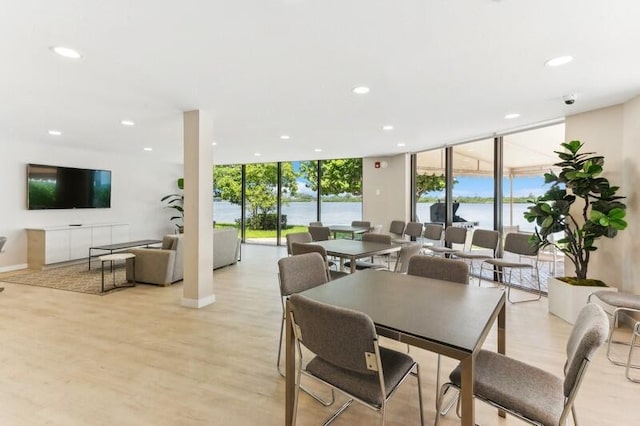 dining area with floor to ceiling windows, light hardwood / wood-style flooring, and a water view