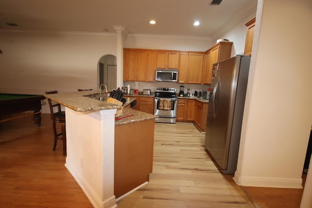 kitchen with appliances with stainless steel finishes, light stone countertops, light hardwood / wood-style flooring, and a breakfast bar area