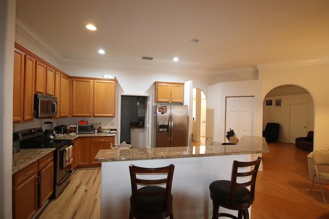 kitchen featuring stone counters, light hardwood / wood-style flooring, appliances with stainless steel finishes, and a center island with sink