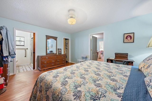 bedroom with a spacious closet, a textured ceiling, ensuite bath, ceiling fan, and light hardwood / wood-style flooring