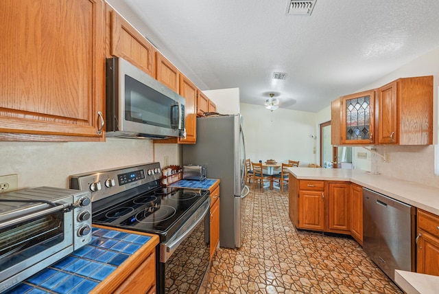 kitchen featuring a textured ceiling, ceiling fan, appliances with stainless steel finishes, and kitchen peninsula