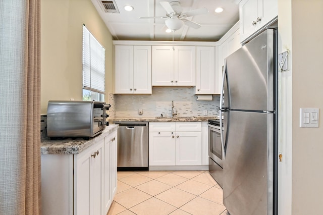 kitchen featuring appliances with stainless steel finishes, tasteful backsplash, light stone counters, sink, and white cabinetry