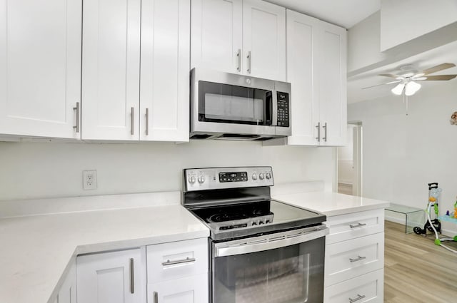 kitchen with light wood-type flooring, white cabinets, light stone counters, ceiling fan, and appliances with stainless steel finishes