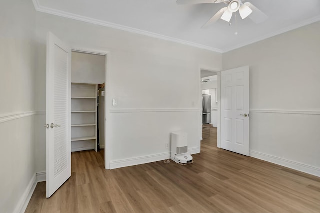 unfurnished bedroom featuring hardwood / wood-style floors, stainless steel refrigerator, crown molding, a walk in closet, and ceiling fan