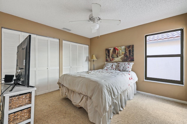 bedroom featuring ceiling fan, a textured ceiling, light carpet, and multiple closets