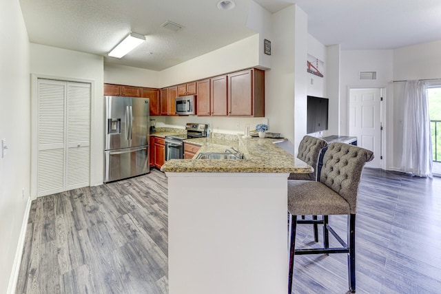 kitchen with a breakfast bar area, stainless steel appliances, light stone counters, kitchen peninsula, and light hardwood / wood-style floors